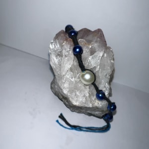 May include: A black cord bracelet with blue and white beads. The bracelet is on a white crystal rock.