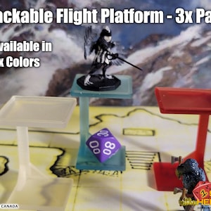 May include: Three stackable flight platforms in clear, blue, and red. The platforms are designed to elevate miniatures for tabletop games. The platforms are made of plastic and have a square base and a single pillar.