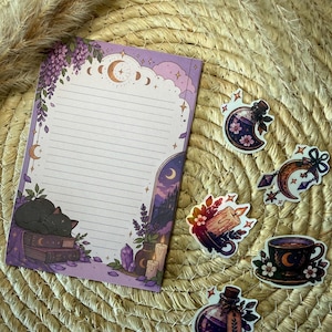 Könnte beinhalten: Ein rechteckiger linierter Notizblock mit violettem Rand, der eine schlafende schwarze Katze auf Büchern, Glyzinien, Kerzen und Kristalle zeigt, begleitet von fünf einzelnen Aufklebern mit einem Zaubertrankfläschchen, einer Mondsichel, einer Kerze und einer Teetasse.