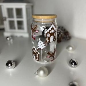 Könnte beinhalten: Ein klares Glasgefäß mit einem Holzdeckel, verziert mit einer Winterszene mit Rentieren und Häusern. Das Gefäß ist mit weißen und braunen Ornamenten gefüllt.