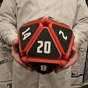 May include: A red and black 20-sided dice with numbers 2, 8, 14, and 20 visible. The dice is made of foam and has a textured surface.