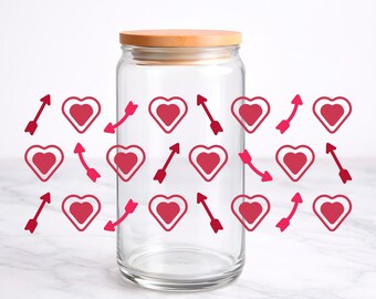 May include: A clear glass tumbler with a bamboo lid, featuring a repeating pattern of dark pink hearts and red arrows printed on the exterior surface. The cylindrical glass container has a smooth, transparent finish and a flat wooden top.