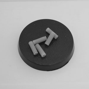 Może przedstawiać: Zbliżenie na pięć małych, szarych, cylindrycznych przedmiotów z tworzywa sztucznego na czarnej powierzchni. Przedmioty są ułożone w losowym wzorze.