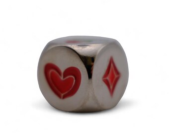 May include: A metallic silver die with red heart and diamond suit symbols. The die is cube-shaped and has a reflective surface, with the symbols painted on the sides. The image is set against a white background.