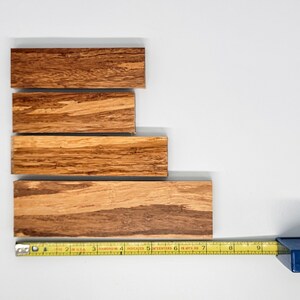 May include: Four wooden strips of varying lengths stacked on top of each other. A yellow measuring tape is placed below the strips, with the numbers 1 through 9 visible.
