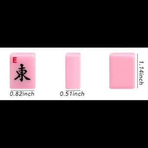 May include: Three pink Mahjong tiles are displayed, showcasing the "East" tile with a black character and the letter "E". Measurements are provided: 0.82 inches wide, 1.14 inches tall, and 0.51 inches thick. The tiles are set against a white background.