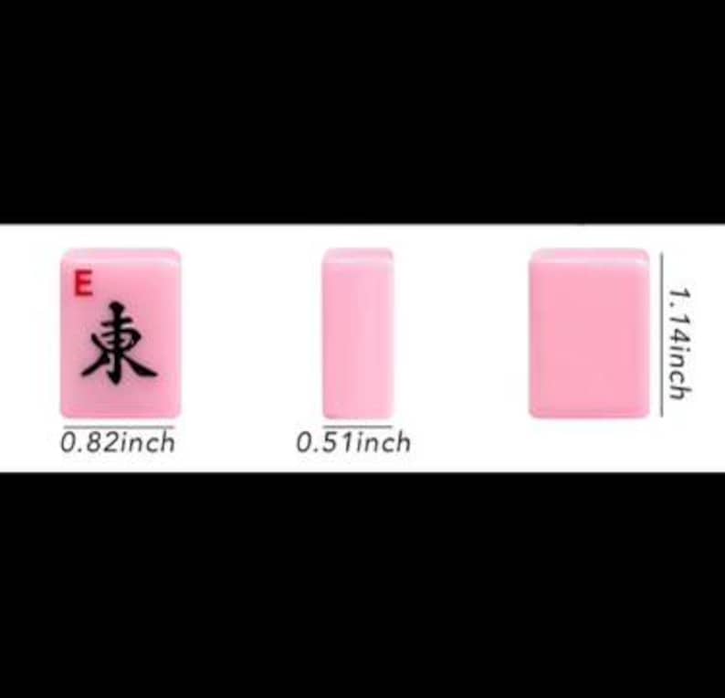 May include: Three pink Mahjong tiles are displayed, showcasing the "East" tile with a black character and the letter "E". Measurements are provided: 0.82 inches wide, 1.14 inches tall, and 0.51 inches thick. The tiles are set against a white background.