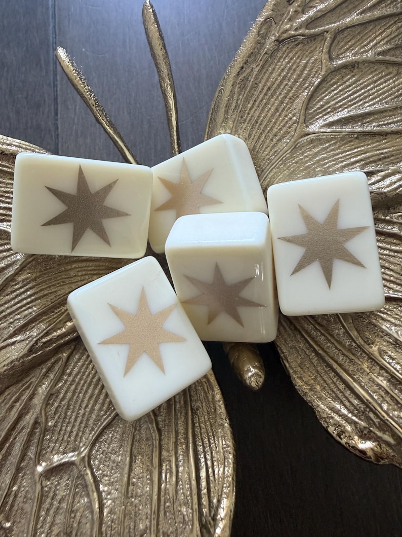 May include: Four rectangular off-white tiles, each featuring a centered metallic gold eight-pointed star design. The tiles are arranged in a cluster, resting upon a textured, metallic gold butterfly-shaped decorative object with detailed wing veins.