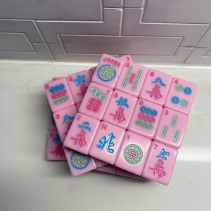 Pu&ograve; includere: Tessere rosa di Mahjong con simboli e caratteri blu, verdi e rossi. Le tessere sono impilate in modo casuale. Alcune tessere hanno la parola "Joker".
