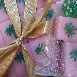 May include: Pink tiles with green palm tree designs are tied with a gold ribbon. A small mesh bag contains additional pink tiles. The tiles are likely part of a game set, possibly Mahjong or a similar tile-based game.