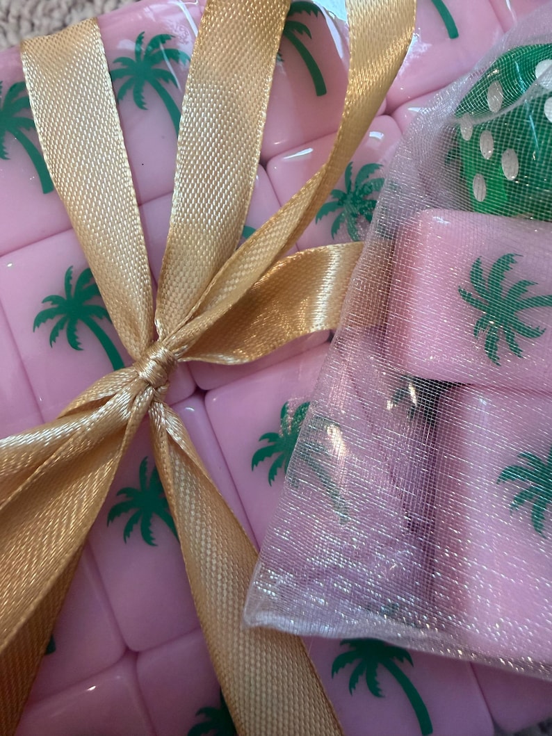 May include: Pink tiles with green palm tree designs are tied with a gold ribbon. A small mesh bag contains additional pink tiles. The tiles are likely part of a game set, possibly Mahjong or a similar tile-based game.
