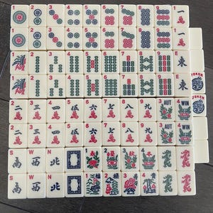 May include: An assortment of ivory-coloured Mahjong tiles, each featuring distinct symbols, numbers, and Chinese characters in red, green, and blue. The tiles are arranged in a grid, displaying the variety of designs and suits.
