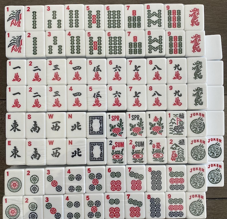 May include: A collection of white Mahjong tiles, featuring red and green symbols and numbers. The tiles display various suits, including characters, bamboos, and circles, along with directional winds and Jokers. A classic game.