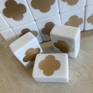 May include: White tiles with a gold clover design. The tiles are arranged in a group, with some standing upright and others lying flat. The gold clover is centered on each tile, creating a simple, elegant pattern. The tiles appear to be made of a smooth, glossy material.