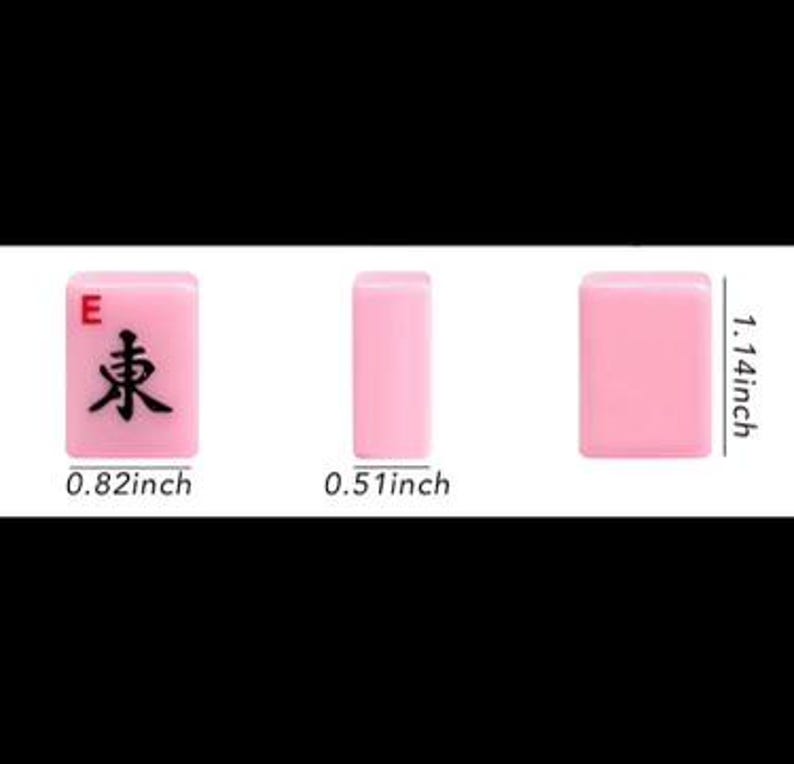 May include: Three pink Mahjong tiles are displayed, showcasing the "East" wind symbol. Measurements are provided: 0.82 inches wide, 1.14 inches tall, and 0.51 inches thick. The tiles are set against a black background.