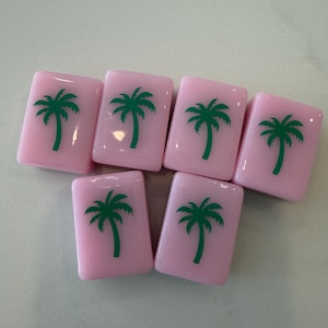May include: Seven pink rectangular tiles with a green palm tree design. The tiles are arranged in a slightly offset pattern, showcasing the repeating tropical motif. The tiles are likely for a game or decorative use.