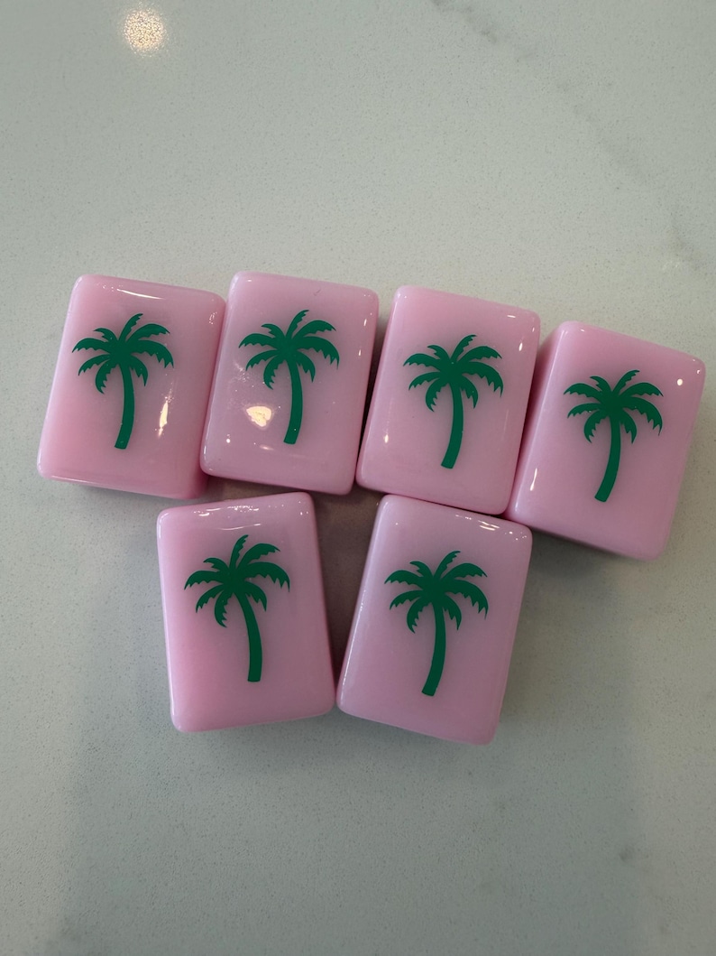 May include: Seven pink rectangular tiles with a green palm tree design. The tiles are arranged in a slightly offset pattern, showcasing the repeating tropical motif. The tiles are likely for a game or decorative use.
