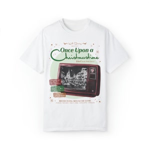Peut inclure: T-shirt blanc avec un motif de télévision rétro affichant le texte "Once Upon a Christmastime" et "Broadcasting Around the Globe". Le motif comprend une scène de Noël et du texte supplémentaire. Un tee-shirt sur le thème des fêtes.