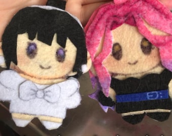 Puede incluir: Dos llaveros de fieltro de personajes con cierres metálicos. Un llavero presenta un personaje con cabello negro y un atuendo blanco. El otro tiene cabello rosa y un atuendo negro. El texto "custom character keychain" está en la parte inferior.