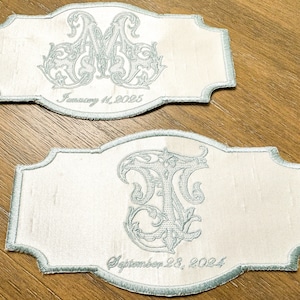 May include: Two embroidered patches with a light blue border and script. One patch features the letters "AM" and the date "January 11, 2025." The other patch has the letters "TF" and the date "September 28, 2024."