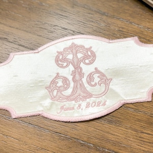 May include: A white embroidered patch with a pink border and a pink floral design. The patch has the text "June 8, 2024" embroidered in pink. The patch is rectangular with a decorative edge.