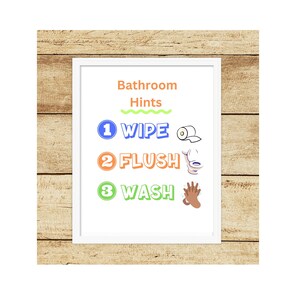 May include: A white framed poster with the text "Bathroom Hints" in orange and green. The poster has three steps for bathroom hygiene: 1. Wipe, 2. Flush, and 3. Wash. Each step has a corresponding icon.