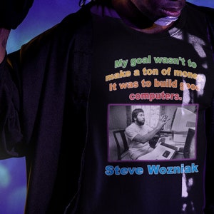 Peut inclure: Un t-shirt noir avec une citation de Steve Wozniak, le co-fondateur d'Apple, imprimée sur le devant. La citation est : "Mon but n'était pas de faire fortune. C'était de construire de bons ordinateurs."