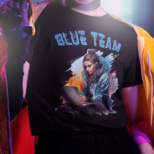 Può includere: Una persona che indossa una maglietta nera con il testo "BLUE TEAM" e una grafica di una donna con le cuffie, che tiene un laptop. Indossa anche una giacca gialla, pantaloni neri e una maschera facciale nera. La persona tiene una pistola nera nella mano destra.
