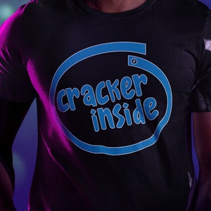 Peut inclure: Une personne portant un t-shirt noir avec un graphique circulaire bleu qui dit "cracker inside". La personne porte des lunettes de protection vert néon et a des dreadlocks.