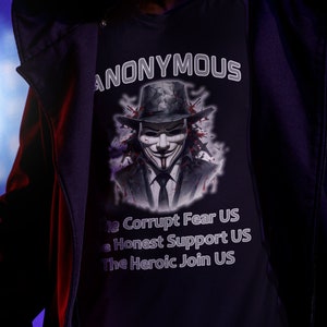 May include: A person wearing a black hooded jacket and a black t-shirt with a graphic of a person wearing a mask and the text "ANONYMOUS" and the text "The Corrupt Fear US The Honest Support US The Heroic Join US".