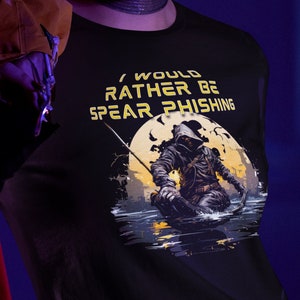 Peut inclure: Un t-shirt noir avec un graphique d'une personne dans une cape à capuche tenant une épée et pêchant dans un lac. Le texte sur le t-shirt est "I would rather be spear phishing".