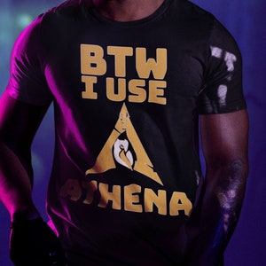 Puede incluir: Una persona con una camiseta negra con el texto "BTW I USE ATHENA" en amarillo. La persona lleva unas gafas de protección verde neón y tiene rastas.