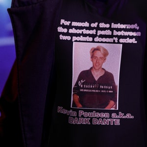 Peut inclure: Une personne portant une veste à capuche noire et un t-shirt noir. Le t-shirt comporte une photo d'un homme et le texte « For much of the internet, the shortest path between two points doesn't exist. » Le texte indique également « Kevin Poulsen a.k.a. DARK DANTE ».