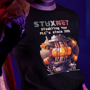 May include: A woman wearing a black t-shirt with a graphic of a machine and the text "STUXNET Disabling your PLC's since 2009".