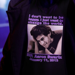 May include: A black hooded sweatshirt with a purple graphic print featuring a photo of Aaron Swartz and the text "I don't want to be happy. I just want to change the world." and "RIP. Aaron Swartz January 11, 2013".