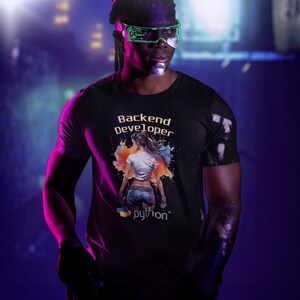 K&ouml;nnte beinhalten: Eine Person tr&auml;gt ein schwarzes T-Shirt mit einer bunten Grafik einer Frau und dem Text "Backend Developer" und "python". Die Person tr&auml;gt eine gr&uuml;ne und schwarze Brille.