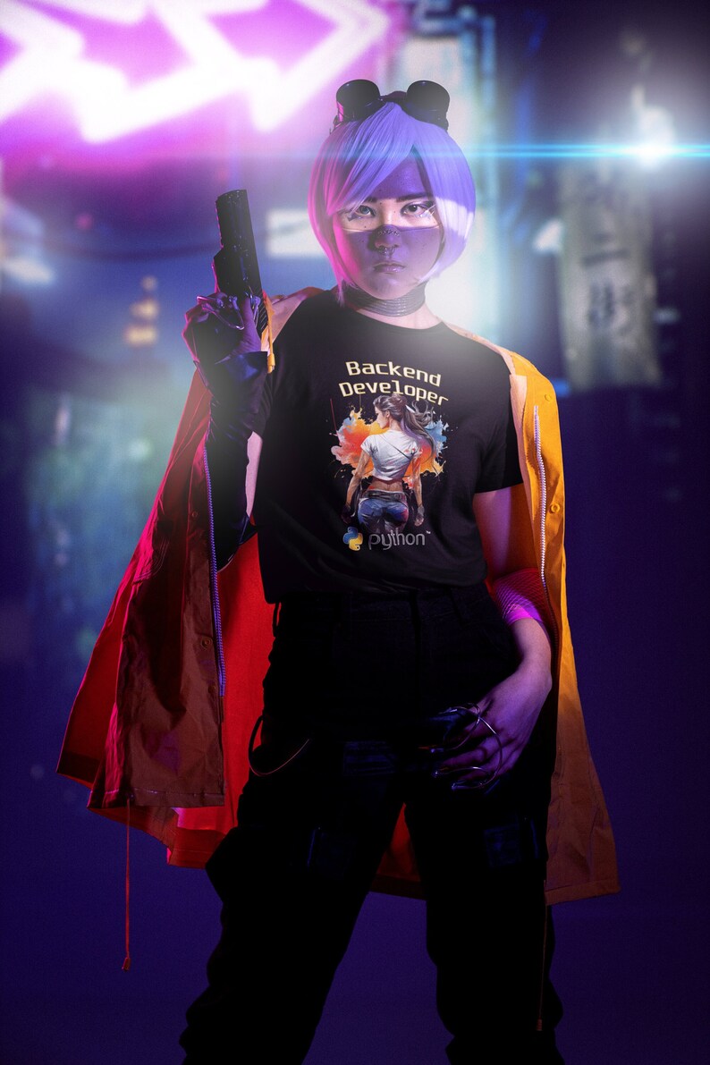 K&ouml;nnte beinhalten: Eine Person tr&auml;gt ein schwarzes T-Shirt mit dem Text "Backend Developer" und einer bunten Grafik einer Person. Das Shirt hat auch ein kleines Python-Logo. Die Person tr&auml;gt eine gelbe Jacke und eine lila Per&uuml;cke. Der Hintergrund ist verschwommen in Lila und Blau.