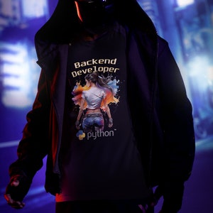 K&ouml;nnte beinhalten: Ein schwarzes T-Shirt mit einer bunten Grafik einer stehenden Frau mit dem Text "Backend Developer" und "python" darunter.