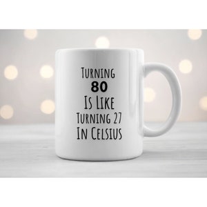 May include: White ceramic mug with black text that reads "Turning 80 is like turning 27 in Celsius".