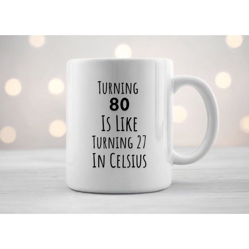 May include: White ceramic mug with black text that reads "Turning 80 is like turning 27 in Celsius".