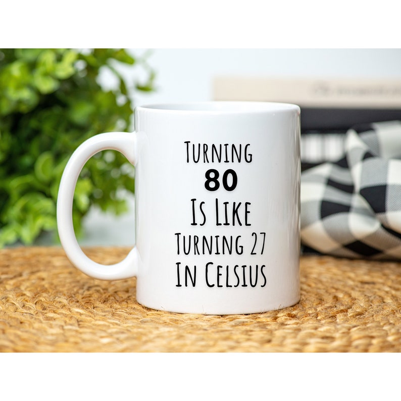 May include: White ceramic coffee mug with black text that reads "Turning 80 is like turning 27 in Celsius".