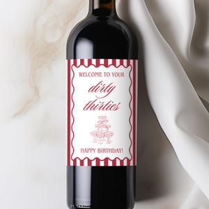 May include: A red wine bottle with a custom label. The label has a white background with a red scalloped border and text that reads "Welcome to your dirty thirties" and "Happy Birthday!" A tiered dessert graphic is also featured.