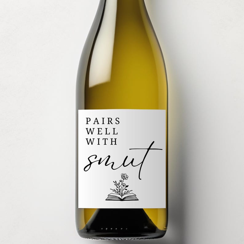 May include: A wine bottle with a white label that reads "PAIRS WELL WITH smut" in black script. The label also features a floral illustration above an open book. The bottle is filled with a light yellow liquid.