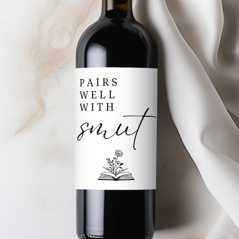 May include: A dark glass wine bottle with a white label. The label reads "PAIRS WELL WITH smut" in black script. Below the text is a small illustration of an open book with flowers.