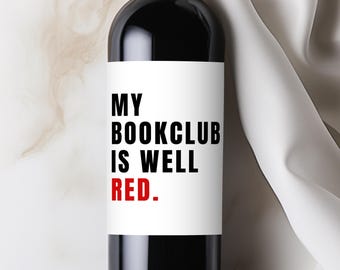 May include: A dark glass wine bottle with a white label. The label reads "MY BOOKCLUB IS WELL RED" in black and red text. The bottle is filled with red wine, and the background is a marble surface.