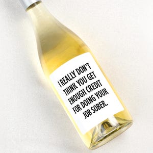 May include: A clear glass wine bottle filled with a pale yellow liquid, featuring a white rectangular label with black text that reads: I REALLY DON'T THINK YOU GET ENOUGH CREDIT FOR DOING YOUR JOB SOBER. The bottle has a silver metallic cap.