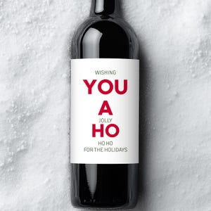 May include: A dark glass wine bottle with a white label. The label has the words "WISHING YOU A JOLLY HO HO HO FOR THE HOLIDAYS" in red and black text. The bottle is set against a white, snowy background.