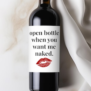 Może przedstawiać: Ciemna butelka wina z białą etykietą. Na etykiecie widnieje napis "open bottle when you want me naked". Pod tekstem znajduje się czerwony odcisk ust. Butelka jest ustawiona na białym tle.