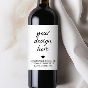 Op de afbeelding: Een donkere wijnfles met een wit etiket. Op het etiket staat "your design here" met een hartsymbool en de tekst "SEND US YOUR DESIGN OR CUSTOMIZE WITH TEXT, ICONS, OR PHOTOS". De fles staat tegen een witte en beige achtergrond.