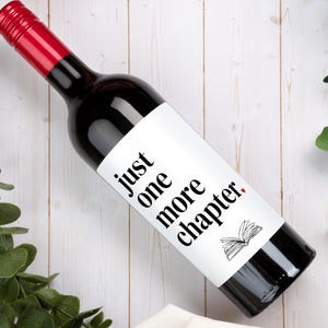 May include: A dark glass wine bottle with a red screw cap and a white rectangular label. The label features the black text "just one more chapter." with a small red heart above the word "chapter." and a black line drawing of an open book.